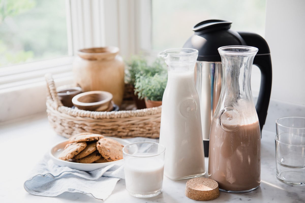 Homemade Dairy-Free Milk with Almond Cow sitting on a table next to a platter of chocolate chip cookies