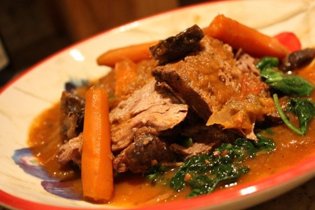 A plate of Beef Pot Roast over a bed of sautéed spinach.