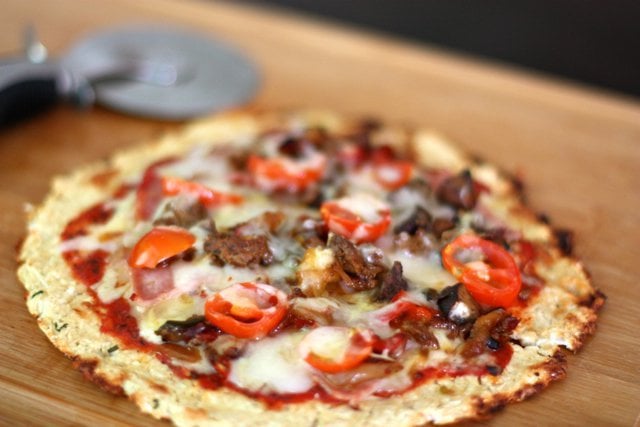 A Cheesy Cauliflower Crust Pizza topped with chorizo sausage, bacon, onions and peppers.