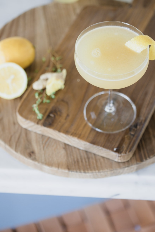 ginger thyme tequila sour served in a glass with lemon garnish on wooden cutting boards 