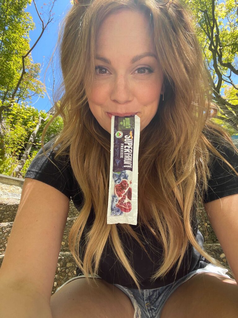 Woman with DeeBee’s Organic Ice Pops in her mouth, taking a selfie 