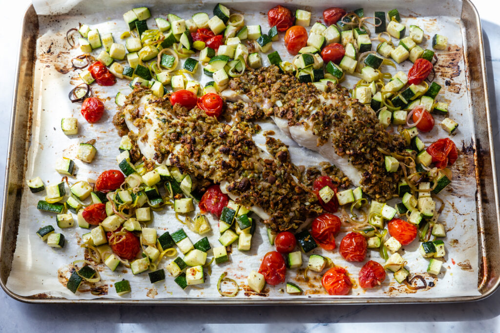 Lemon-Herb crusted halibut baked on a parchment lined sheet pan with roasted vegetables 