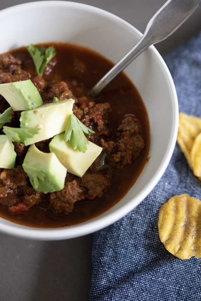 Whole30 recipes like Danielle Walker's chili in a white bowl topped with avocado and cilantro. Plantain chips are on the side