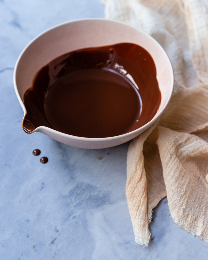 chocolate drizzle in a bowl slight dripping on a marble counter top