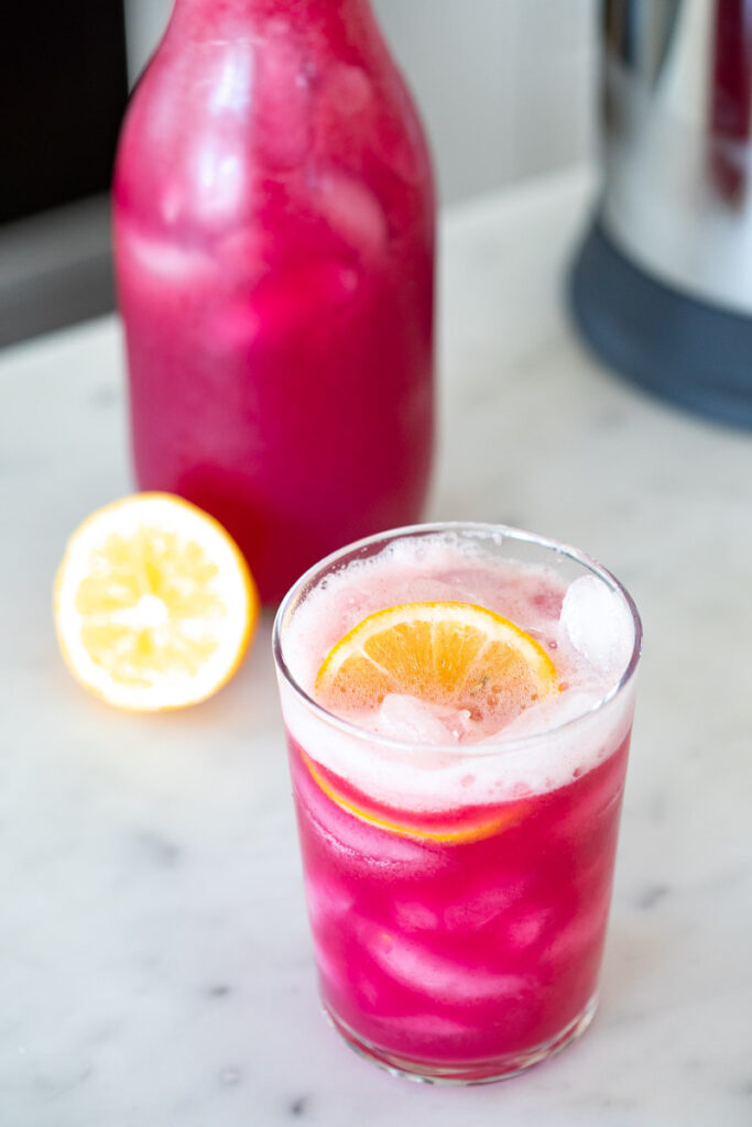 Wild Blueberry Lavender Lemonade in a glass cup full of ice with a lemon garnish sitting on a counter