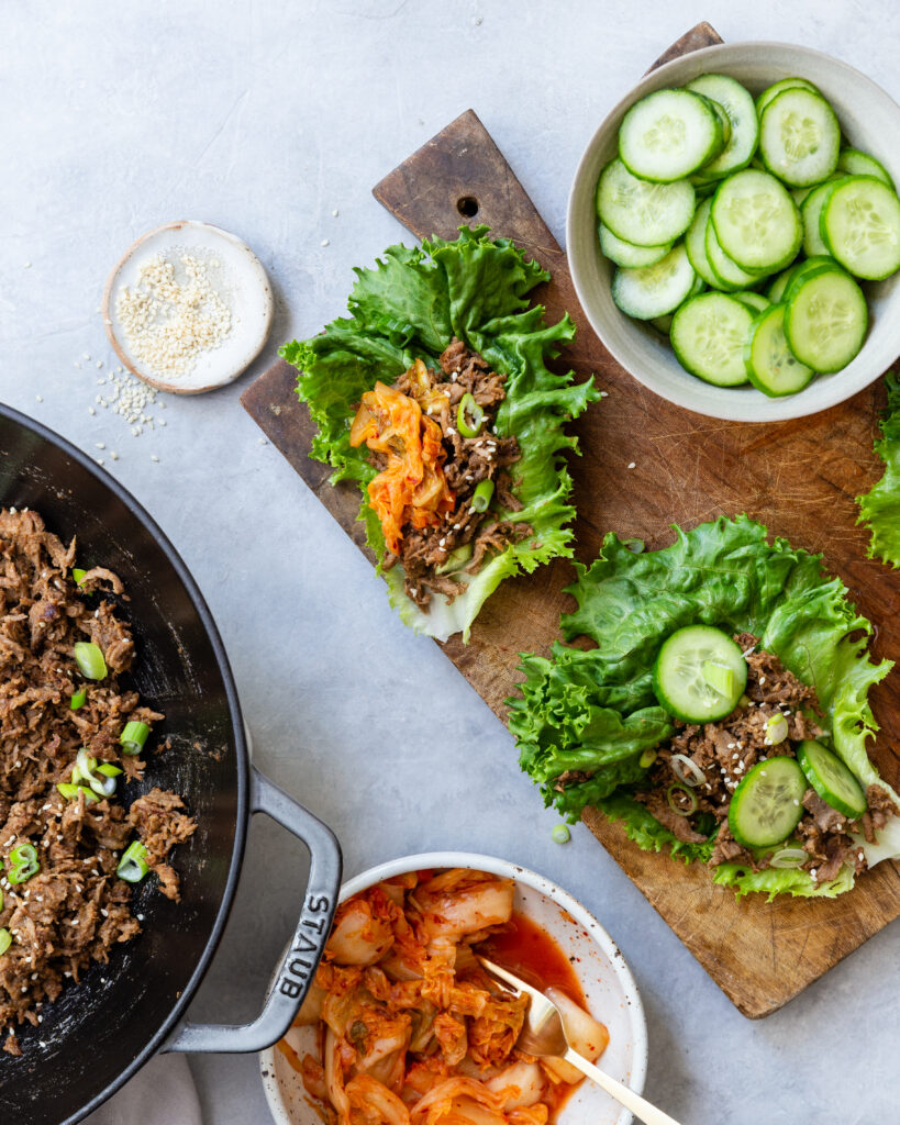 Paleo Beef Bulgogi in lettuce cups on a wooden cutting board with a variety of toppings