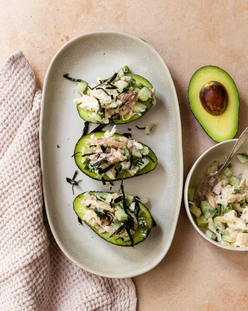 image of gluten free california roll stuffed avocados on a plate next to an avocado
