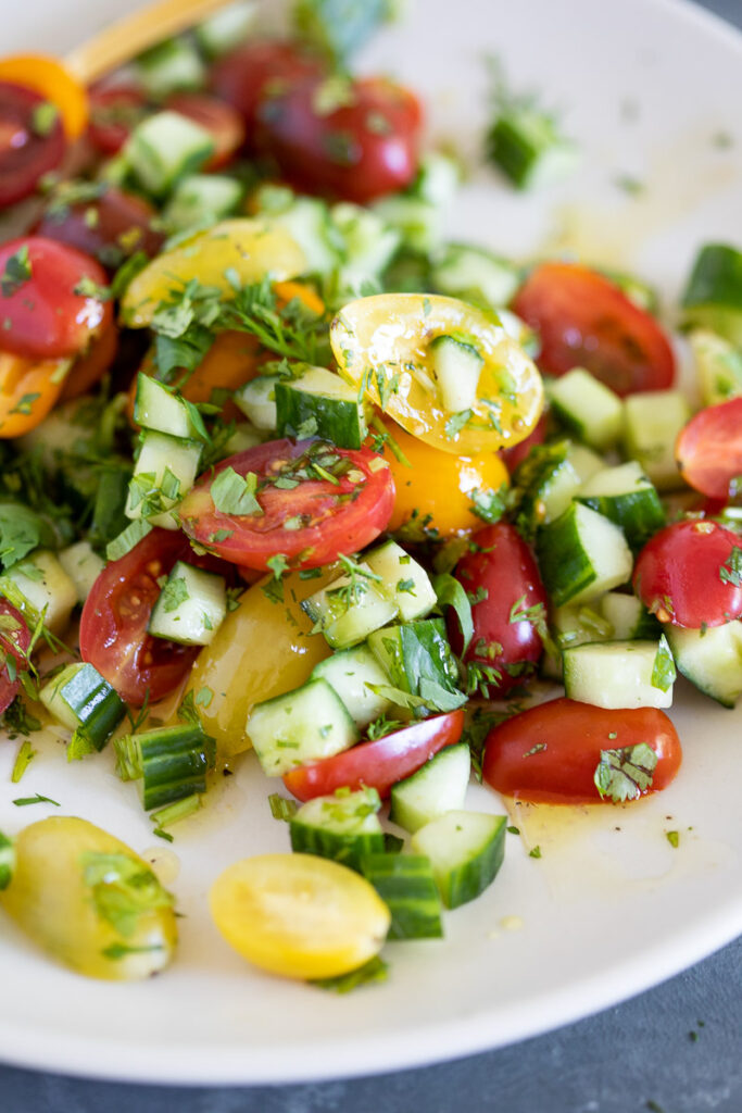 Bright and colorful Tomato Cucumber Salad on a white plate on gray marble table with a gold spoon