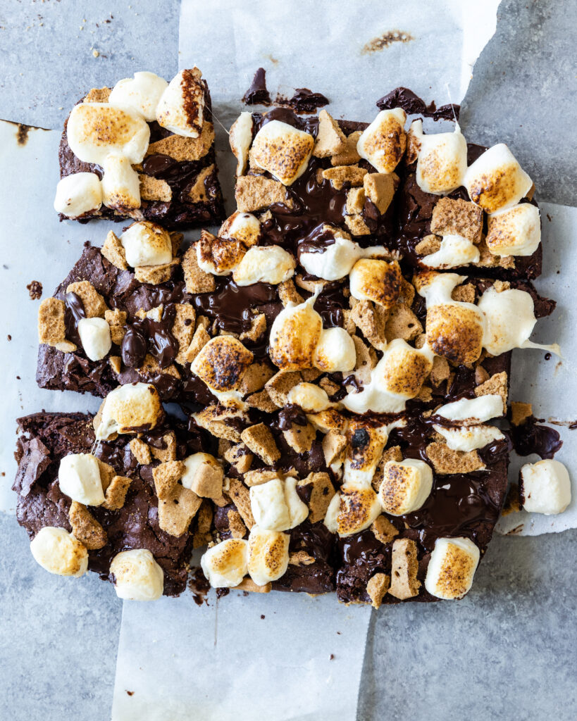 A decadent gluten-free s'mores brownie cut into squares, laying on parchment paper