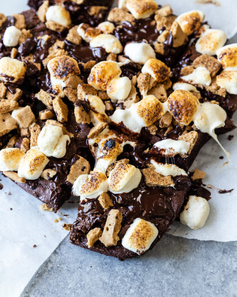 A decadent gluten-free s'mores brownie cut into squares, laying on parchment paper