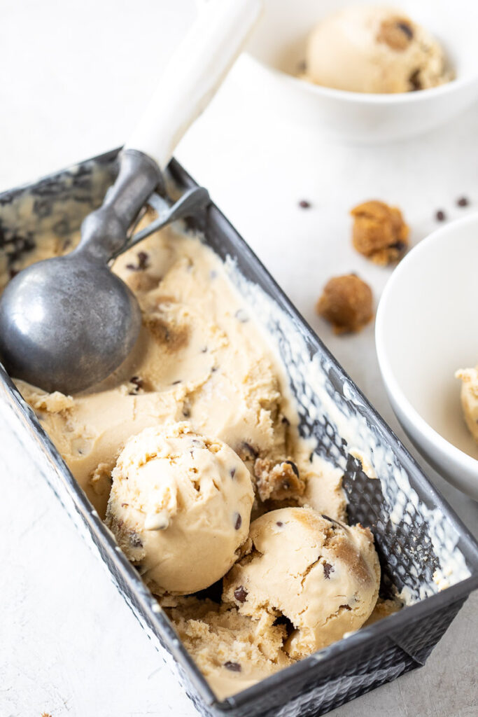 Scoops of Dairy-Free Chocolate Chip Cookie Dough Ice Cream in a metal tin with an ice cream scooper