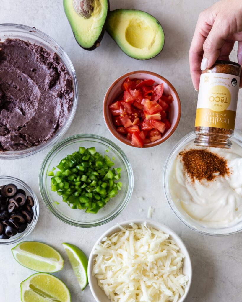 a variety of ingredients to create a grain free 7 layer taco dip in glass bowls and taco seasoning from healthy in a hurry