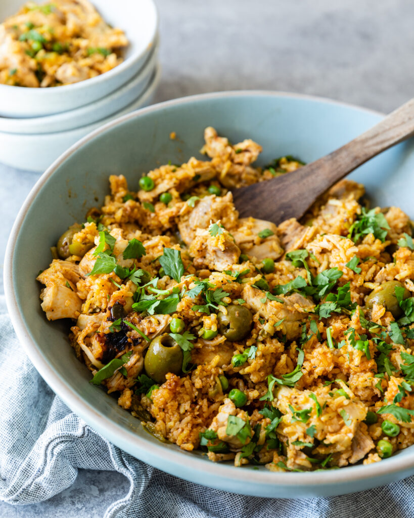 Instant Pot Arroz con Pollo in a light blue bowl ready to serve with a wooden spoon sitting on a counter