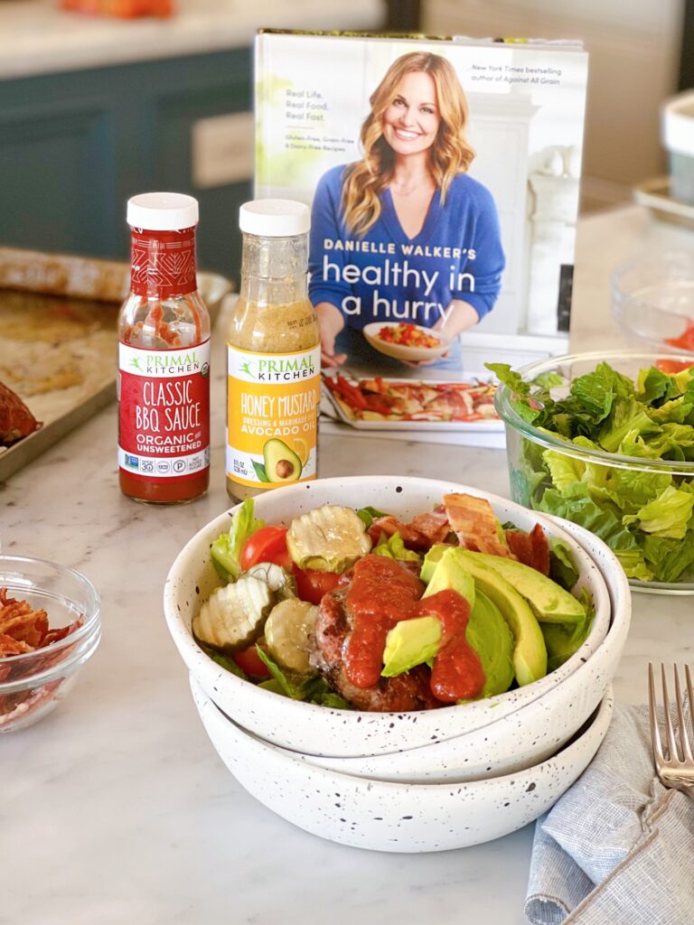 Paleo BBQ Bacon Burger Bowls on a counter with Healthy In a Hurry and Primal Kitchen sauces on display