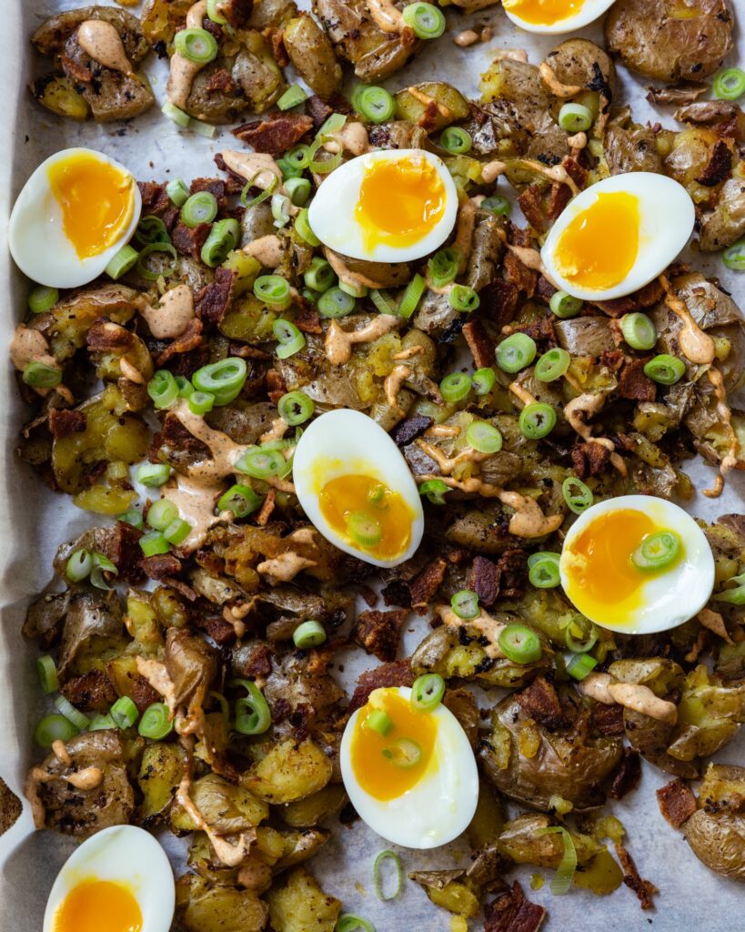 A close up image of Smashed Potatoes with Bacon, Eggs and Spicy Aioli on a sheet pan