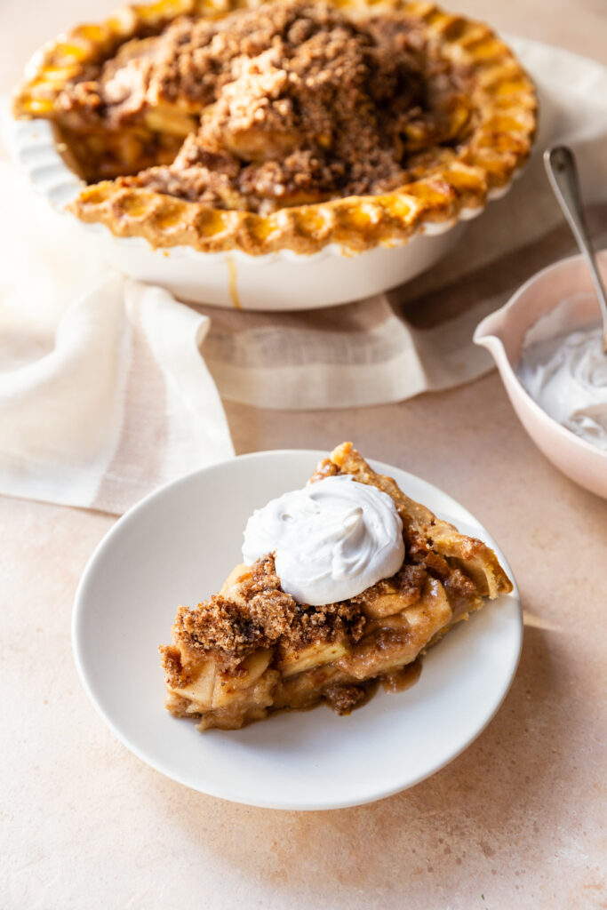 Slice of Gluten-Free Dutch Apple Pie on a small white plate with a dollop of coconut whipped cream on top. 