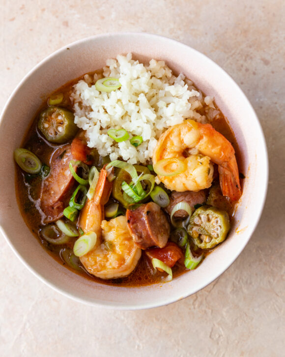 Small white bowl filled with Shrimp & Sausage Stew paired with cauliflower rice rests on a beige counter 