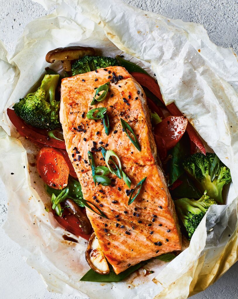 tender Teriyaki Salmon is nestled amongst a medley of vegetables in a packet made of parchment paper 