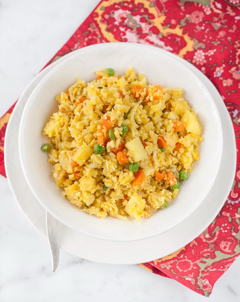 Cauliflower rice vegetable biryani is pictured in this image. The rice is in a white bowl on a white platter. 