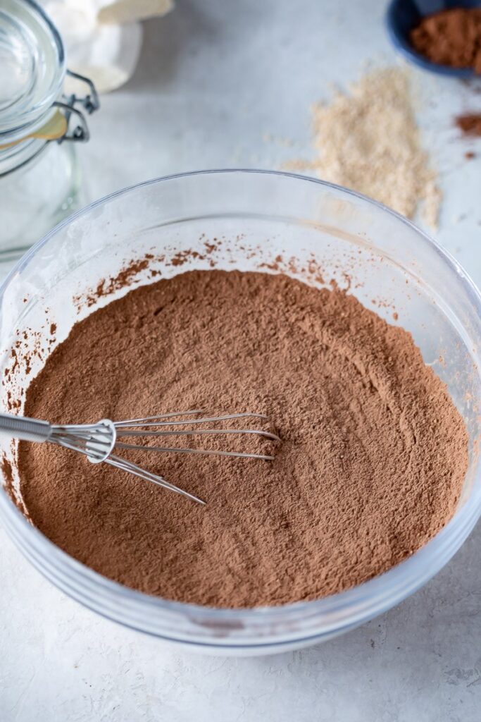 Clear glass bowl with dairy free hot cocoa mix and one whisk 