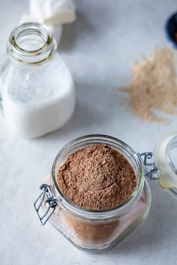 dairy free hot cocoa mix shown in a glass airtight container with a glass bottle of dairy free milk nearby