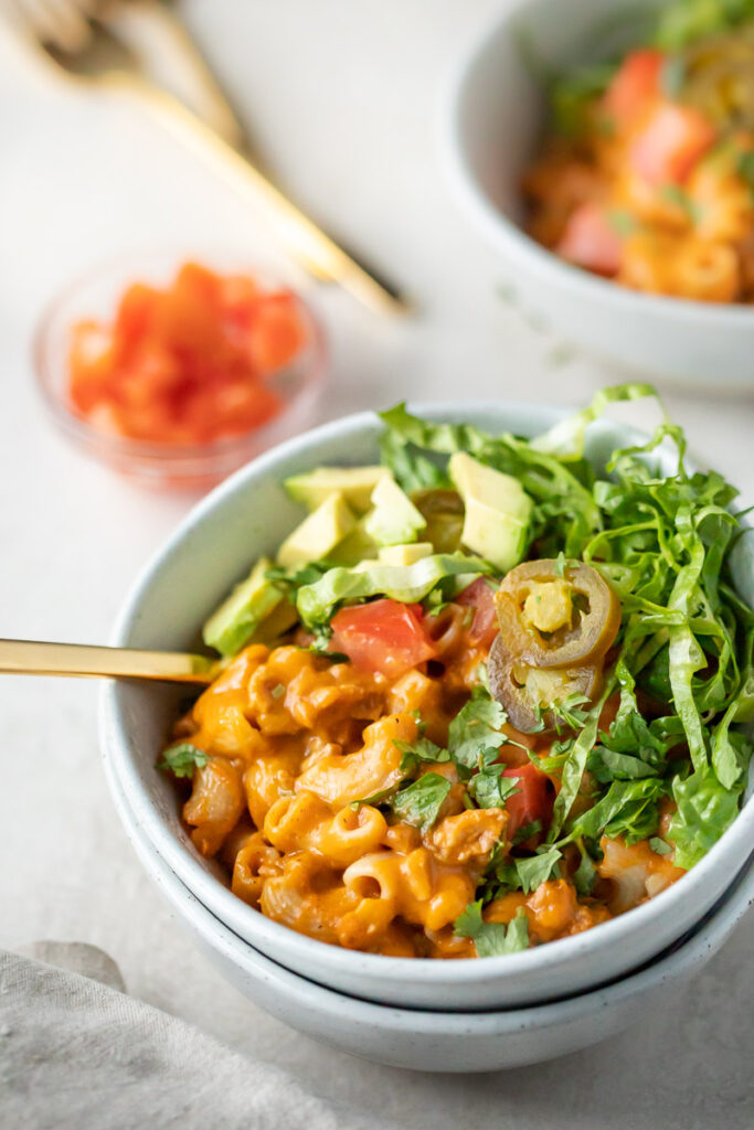 Dairy-Free Instant Pot Taco Pasta pictured in white bowls with a variety of toppings such as jalapenos, avocados, lettuce and tomatoes