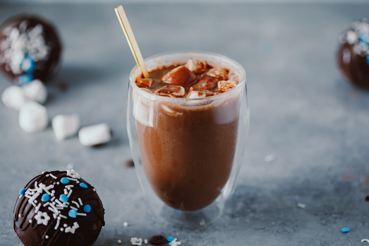 Hot cocoa with marshmallows in a glass cup with cocoa bombs next to it