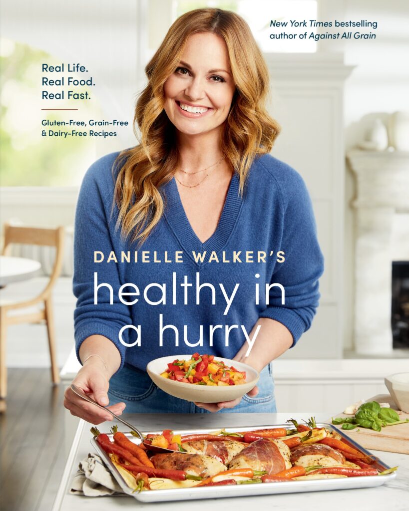 The cover for Healthy In a Hurry featuring Danielle Walker on the cover in a blue sweater smiling at the camera while serving a chicken recipe