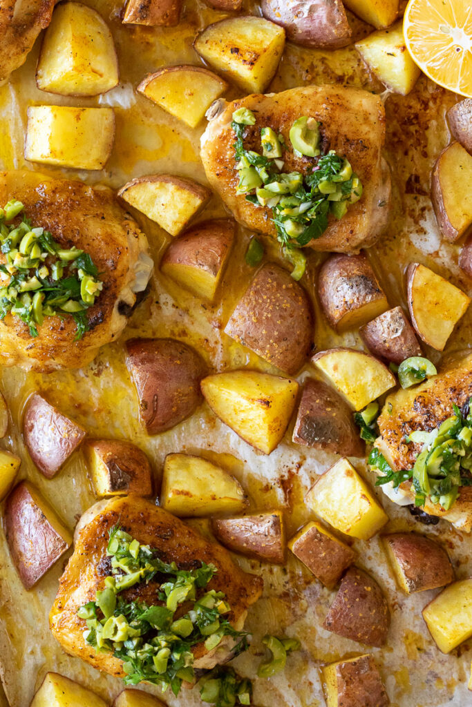 image of roasted chicken thighs and potatoes on a sheet pan with lemon olive salsa on top.