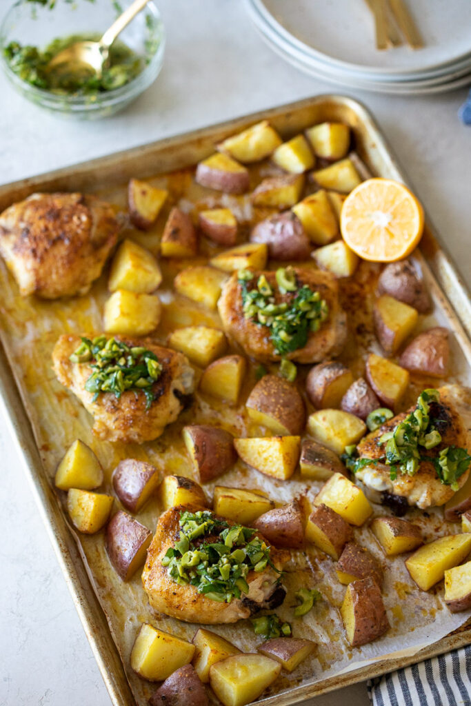 image of roasted chicken thighs and potatoes on a sheet pan with lemon olive salsa on top.