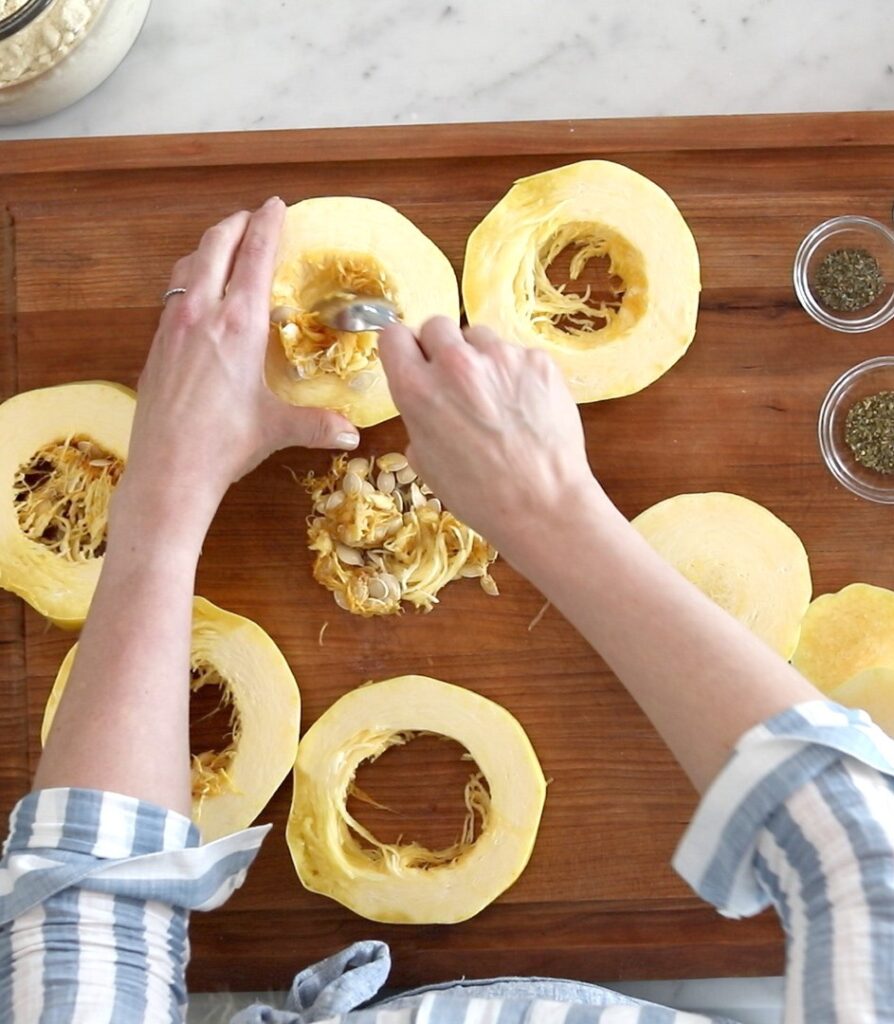 caucasian female hands work on scooping out seeds of cut spaghetti squash rounds