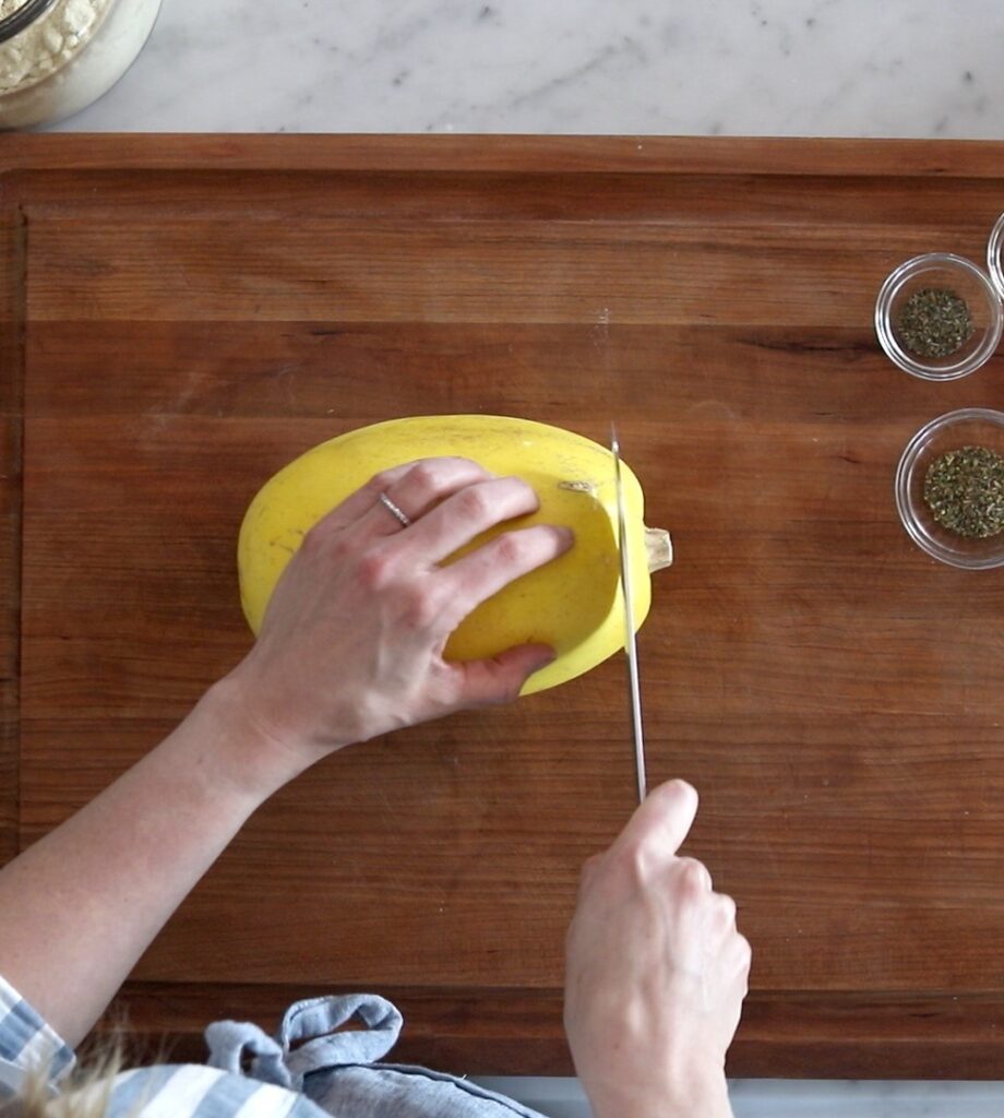 caucasian female hands hold a spaghetti squash and knife on a wooden cutting board 