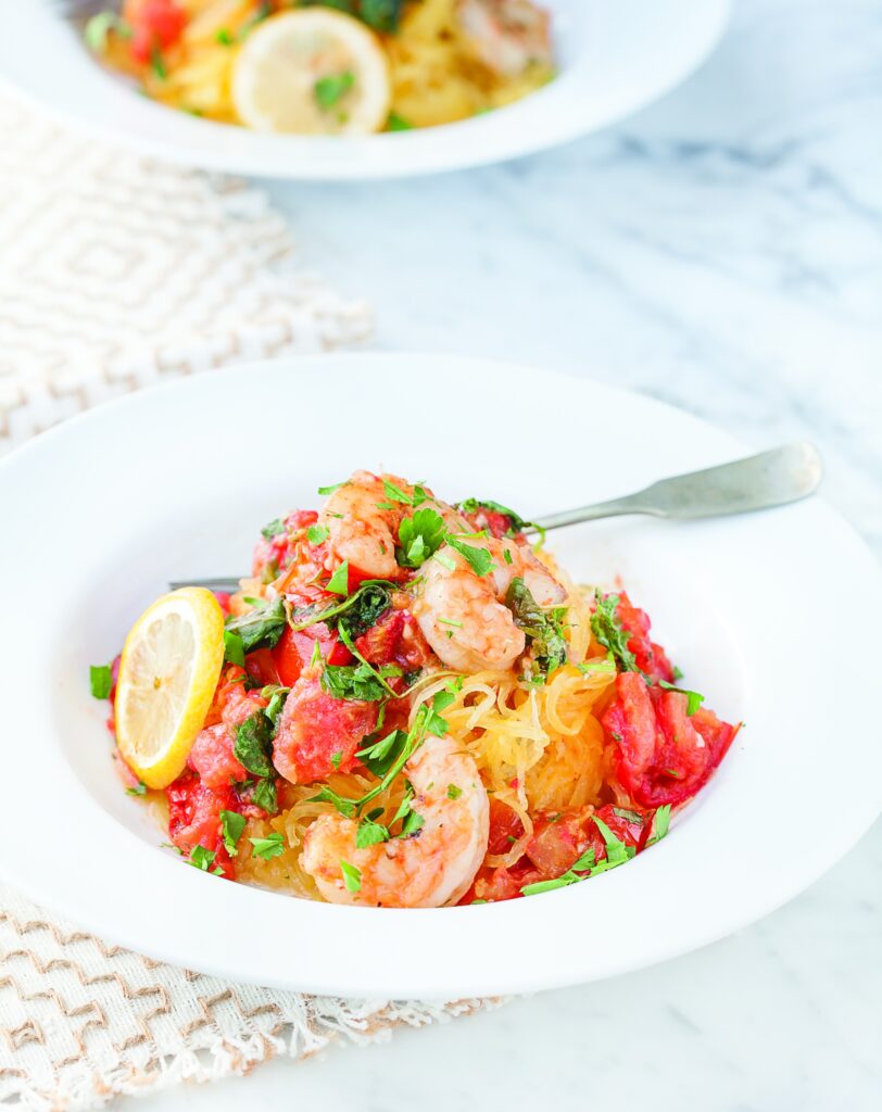 shrimp and tomato pasta served over spaghetti squash in a white bowl with a silver fork