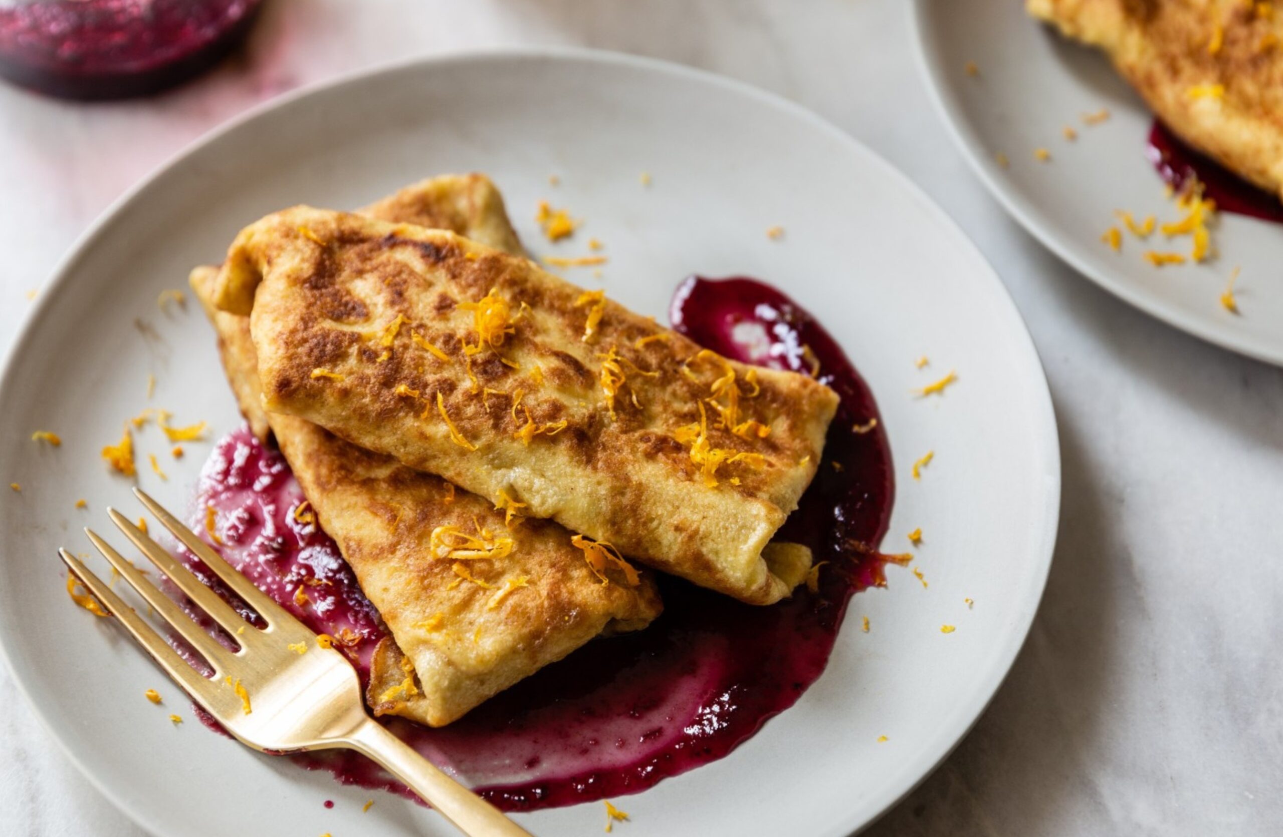 image of dairy free cheese blintz with lemon curd and blueberry on a white plate on a table