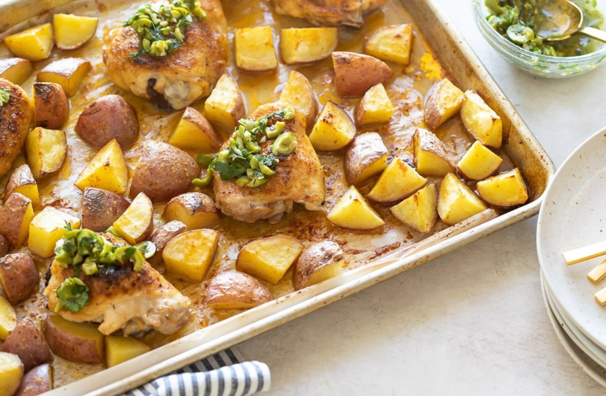 image of chicken tray bake chicken thighs and roasted potatoes on a sheet tray with lemon olive salsa on top