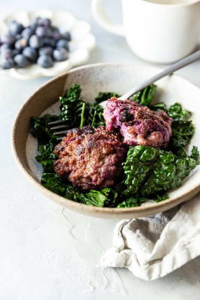 Blueberry Breakfast Sausage Patties on a bed of sauteed greens in a white bowl with a silver fork