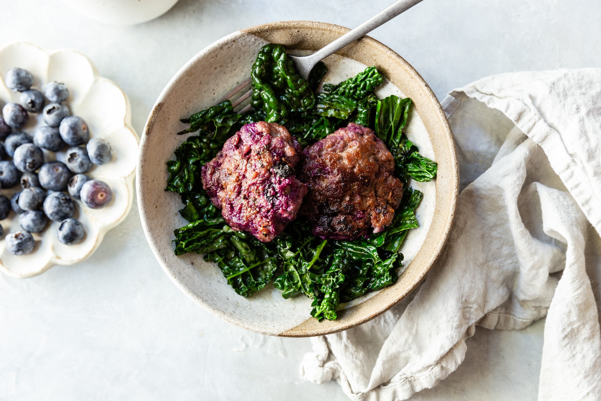 image of blueberry breakfast sausage patties on a bed of kale in a bowl with a fork.