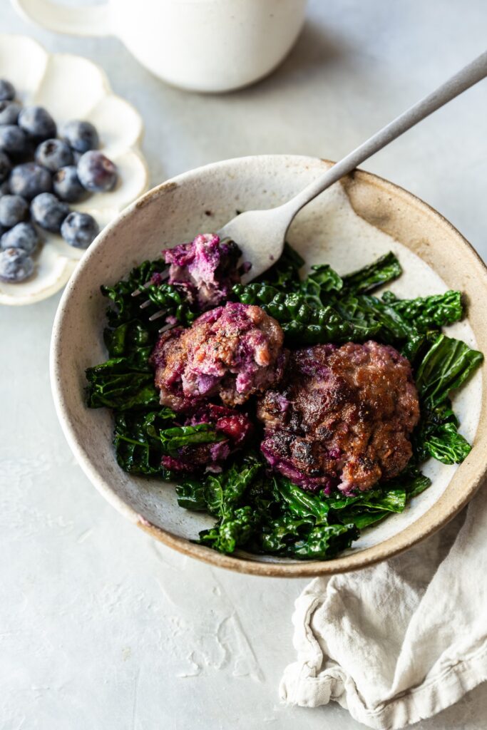 Blueberry Breakfast Sausage Patties on a bed of sauteed greens in a white bowl with a silver fork