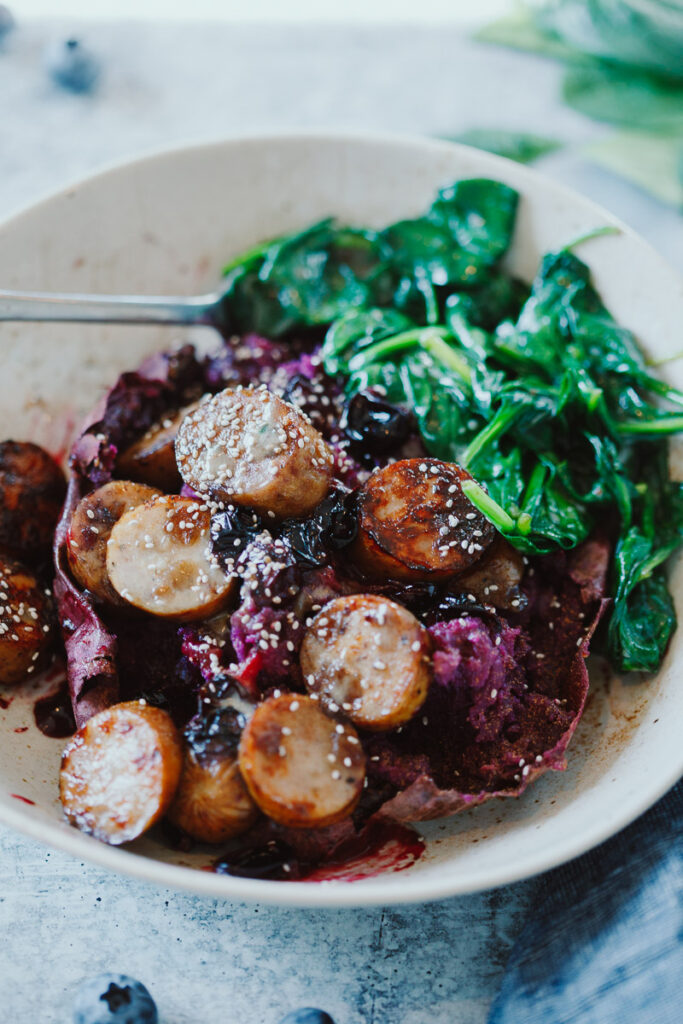 image of purple stuffed breakfast sweet potatoes with chicken sausage and wilted spinach in a bowl.