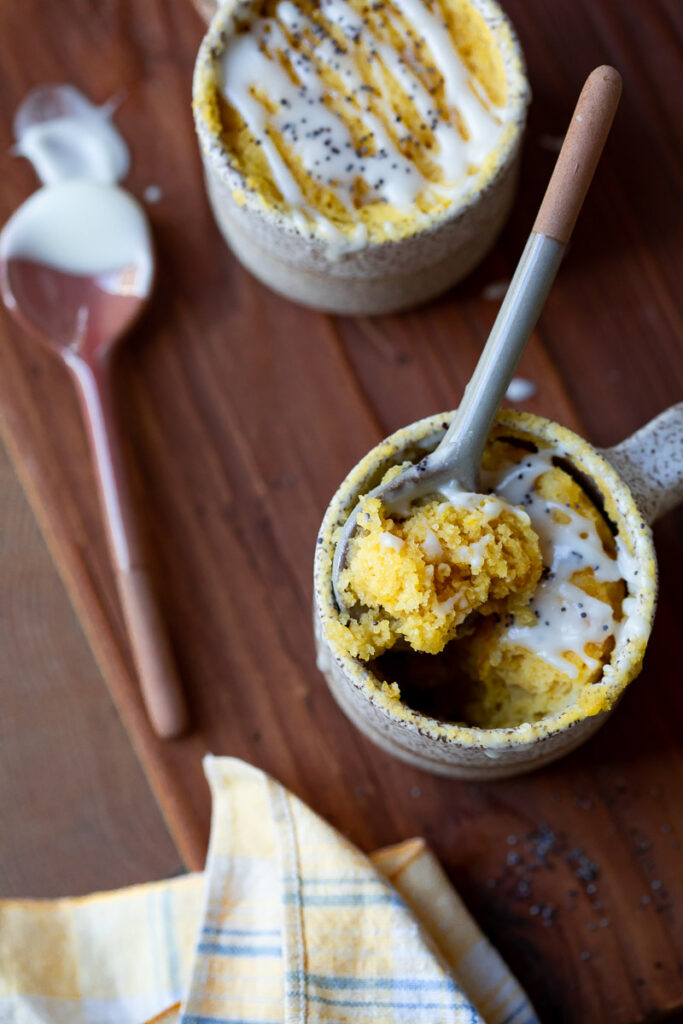 image of two gluten free lemon mug cakes on a counter one with a spoon scooping some out