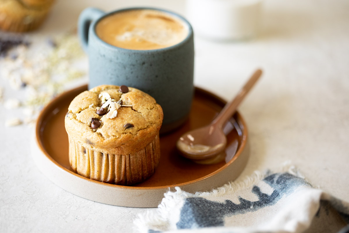 image of a gluten free banana protein muffin on a plate with a cup of coffee