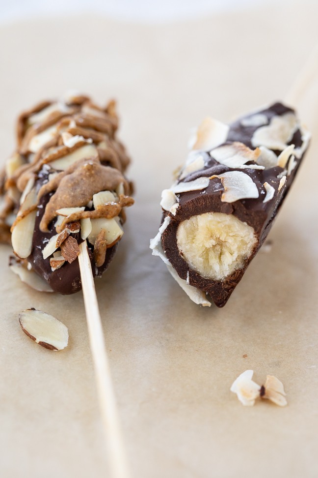image of chocolate covered frozen bananas with coconut and almonds laying on a table