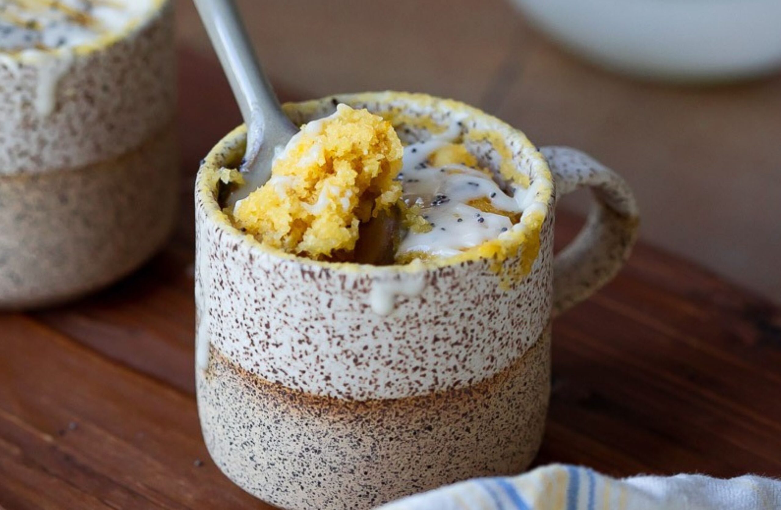 image of gluten-free lemon mug cake in a mug with a spoon on a table