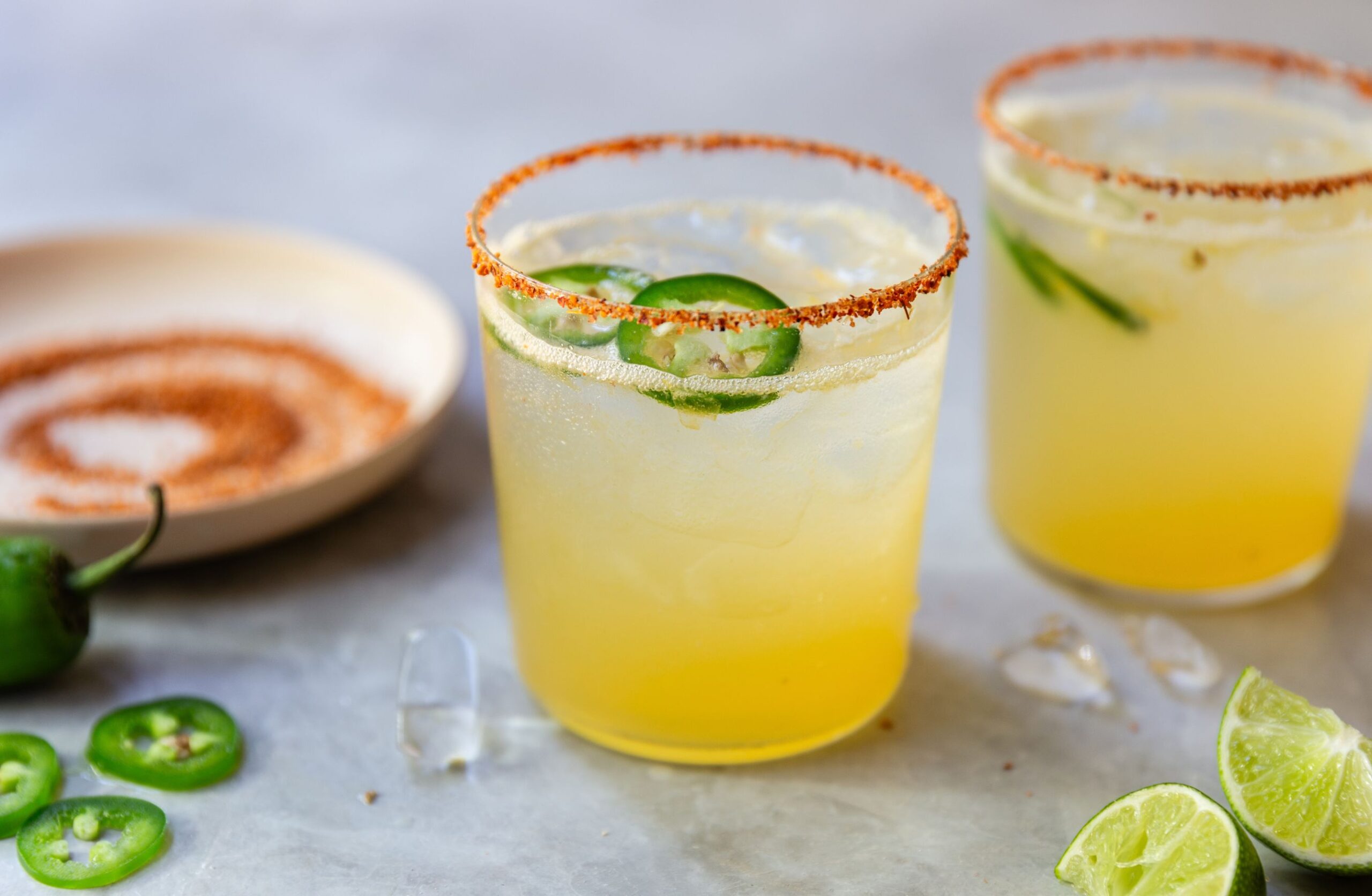 image of two margarita mocktails with tajin rims and limes and jalapenos on a counter