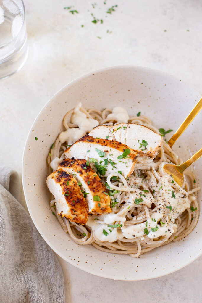 Roasted Garlic Cottage Cheese Alfredo with Blackened Chicken in a white bowl on a counter top.