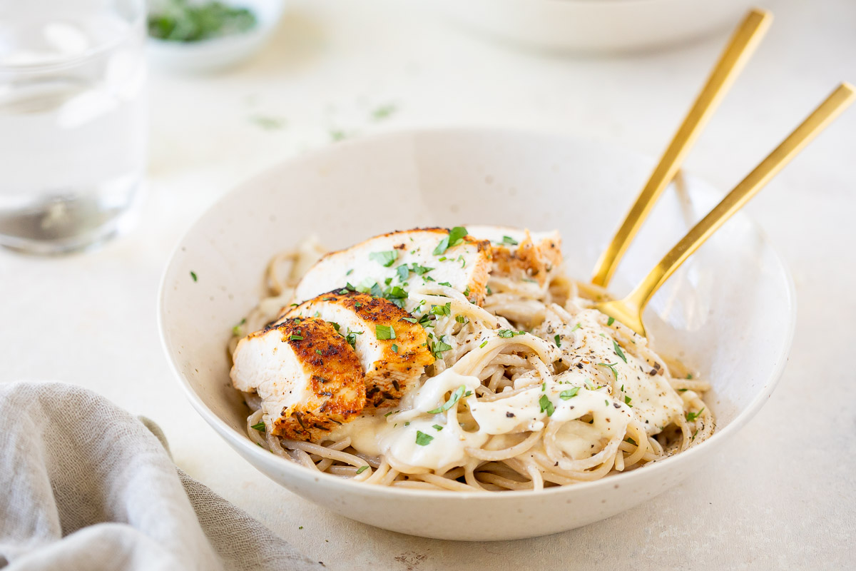 Roasted Garlic Cottage Cheese Alfredo with Blackened Chicken in a white bowl on a counter top.