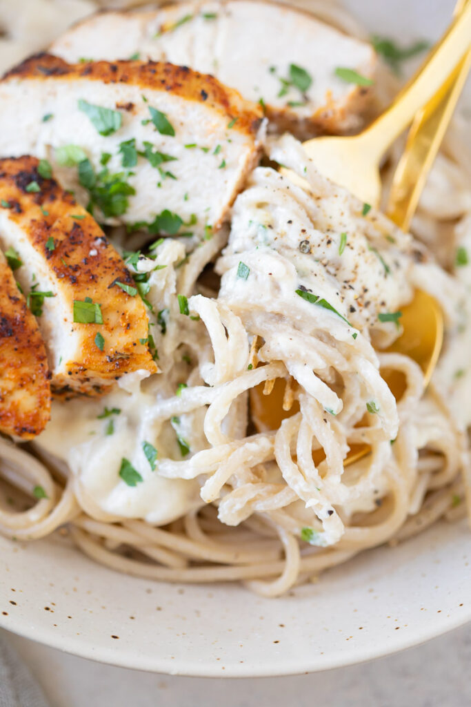 Roasted Garlic Cottage Cheese Alfredo with Blackened Chicken in a white bowl on a counter top.