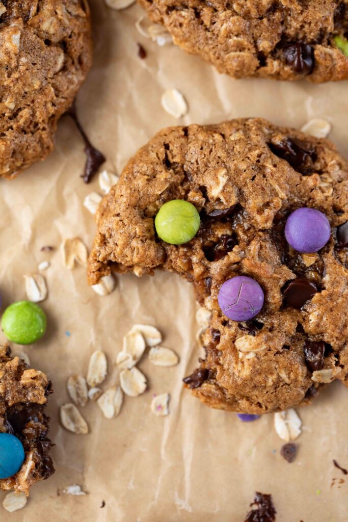 image of gluten-free monster cookie with a bite taken out with dye free candies in a piece of parchment paper