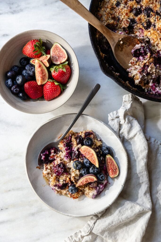 high shot of paleo oatmeal with berries and figs in a white bowl next two a bowl of berries and figs allo n a counter